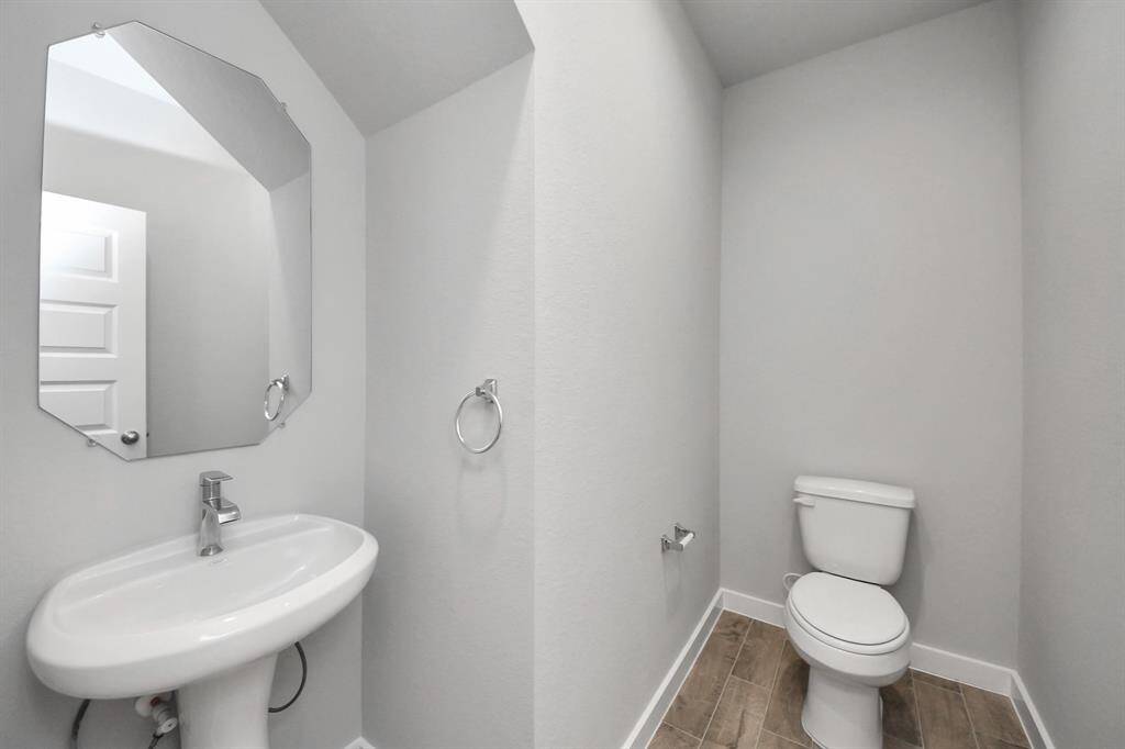 This half bathroom features a stylish pedestal sink, modern hardware, and bright recessedlighting, creating a sleek and inviting space.