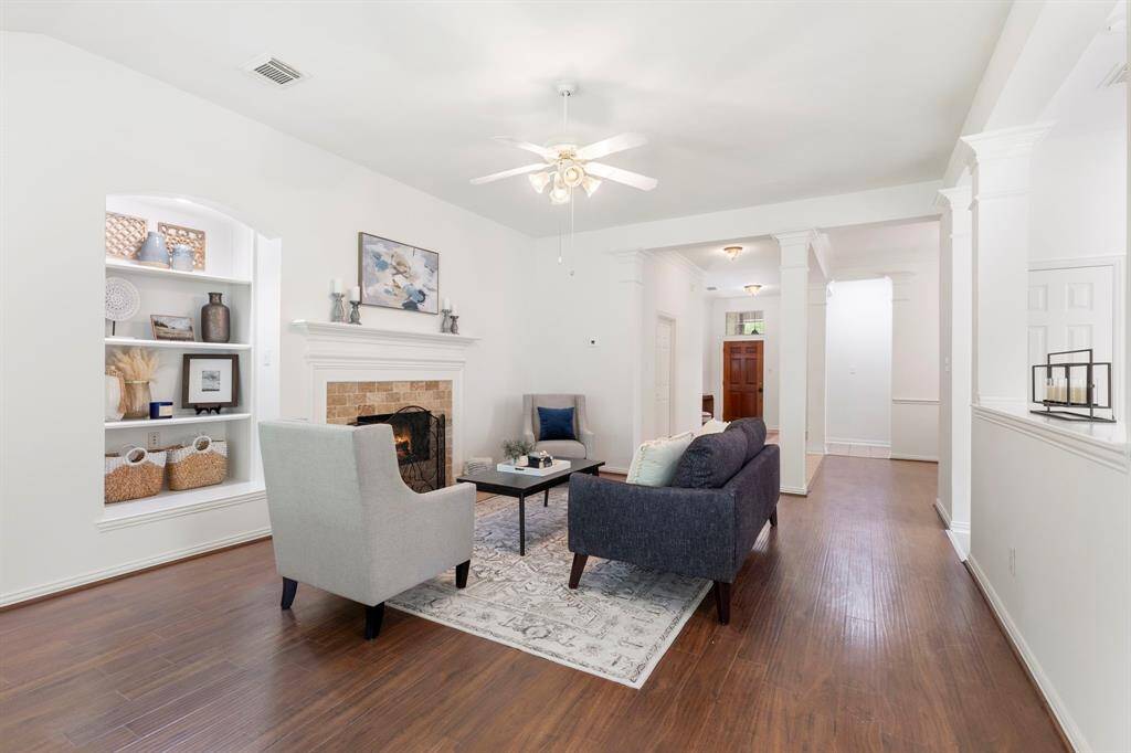This inviting family room features a fireplace, built-in shelving, and elegant hardwood floors. The neutral color palette and ceiling fan enhance the bright, airy atmosphere, perfect for relaxing or entertaining.