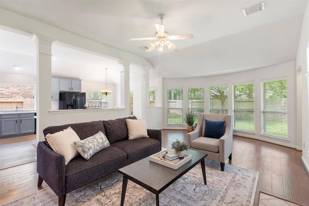 Bright and inviting family room with large windows offering plenty of natural light. Features an open layout connecting to the kitchen, hardwood floors, and a ceiling fan. Ideal for comfortable living and entertaining.