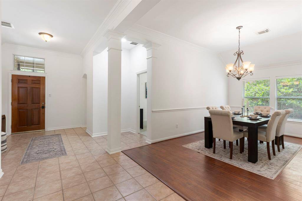 This photo features a bright entryway with tile flooring, leading to an elegant dining area with hardwood floors. The dining room is well-lit with a stylish chandelier and large windows, offering a view of the outdoors. The space is open and welcoming, perfect for entertaining.