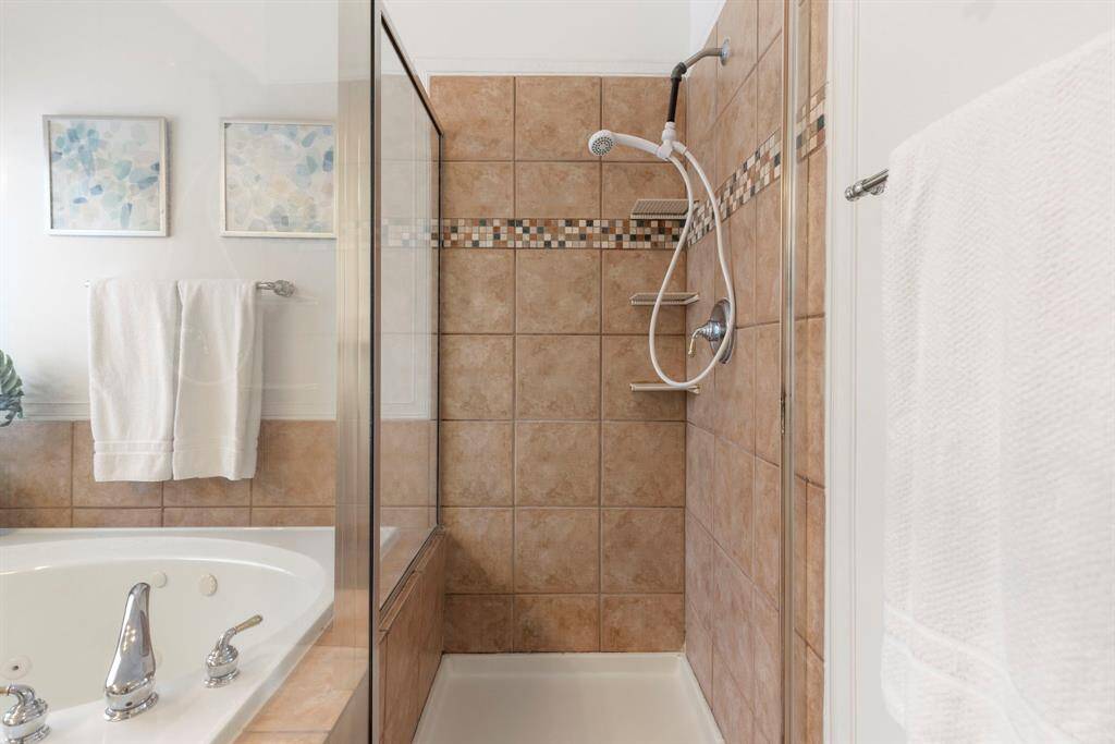 This bathroom features a separate shower with tiled walls and a decorative mosaic border, alongside a luxurious corner bathtub,  creating a relaxing atmosphere.