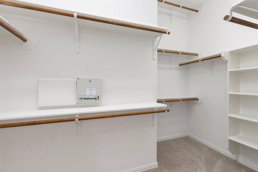 Spacious walk-in closet with multiple wooden hanging rods and shelves, offering ample storage and organization options. The neutral color scheme provides a clean and versatile backdrop.