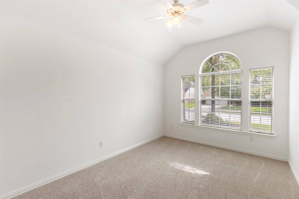 Bright and airy secondary bedroom with vaulted ceiling, carpeted floor, and a large arched window offering ample natural light and a view of the outdoors.