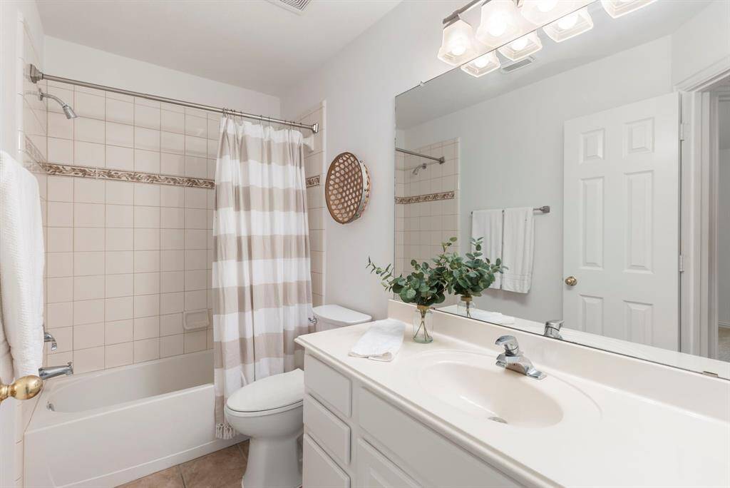 Bright and clean bathroom featuring a tiled bathtub with a shower, a large mirror above a single-sink vanity, and modern lighting.