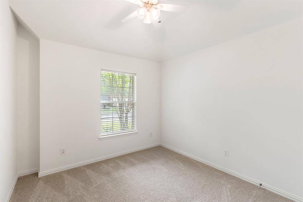 Bright, carpeted secondary bedroom with neutral walls, a single window providing natural light, and a ceiling fan for comfort.