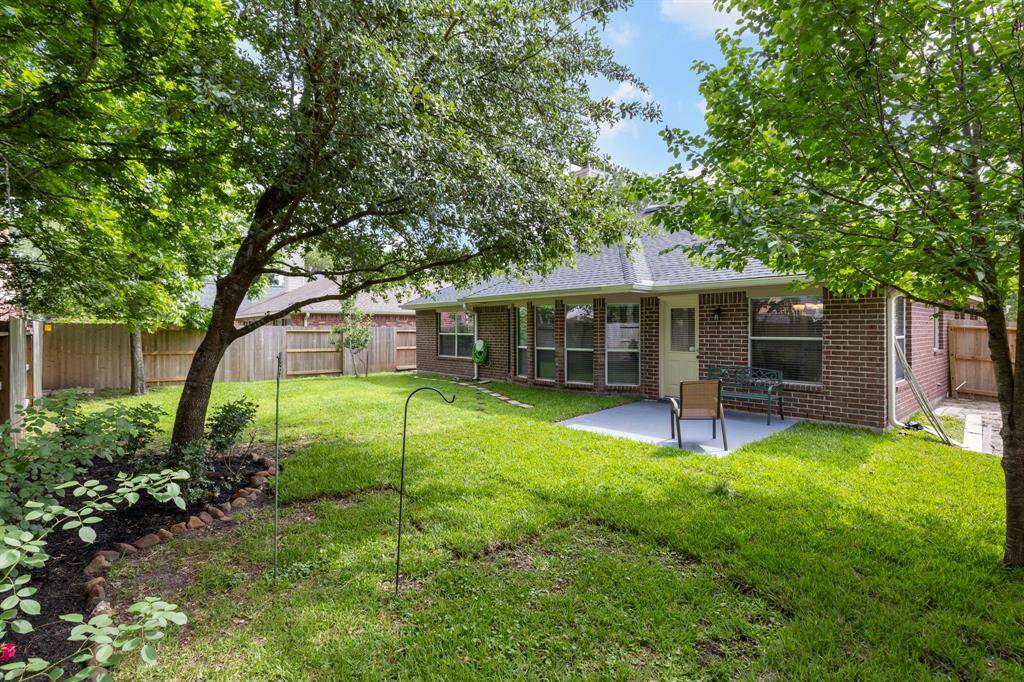 Charming backyard featuring a well-maintained lawn, mature trees, and a cozy patio area perfect for relaxation or entertaining. The space is enclosed with a wooden fence, offering privacy and a serene atmosphere.