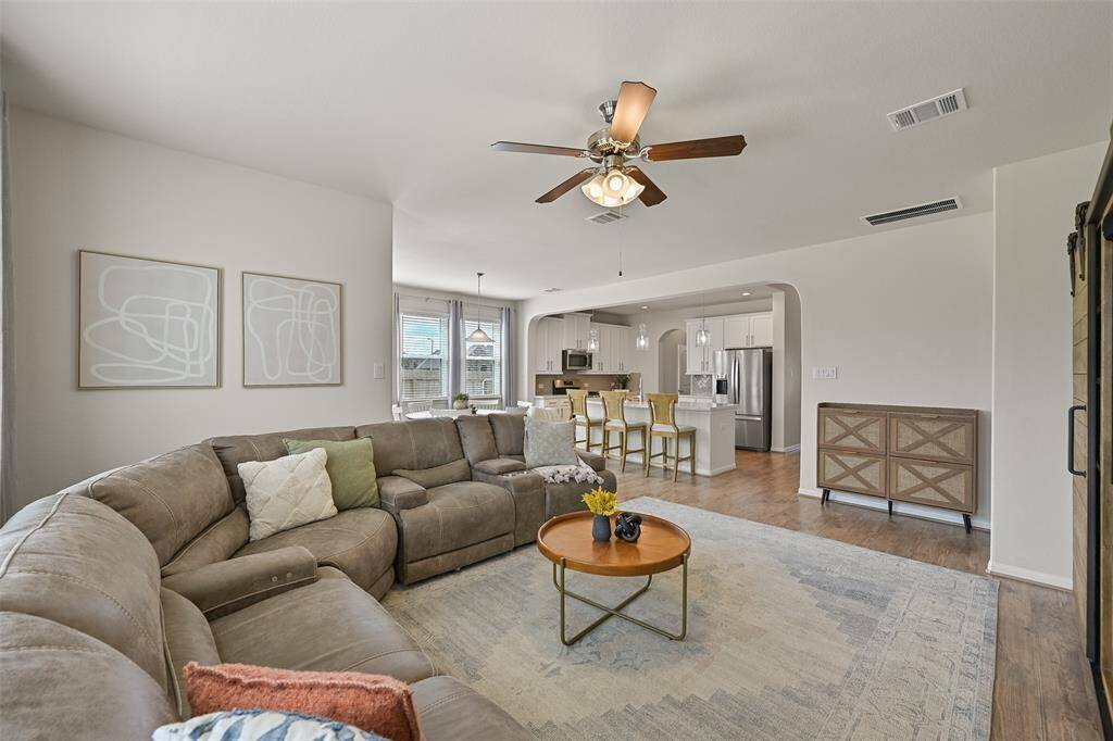 Get cozy and comfortable in this inviting family room at the rear of the home. This space showcases a lighted ceiling fan, luxury vinyl plank floors, neutral paint, & a wall of rear-facing windows shaded by 2-inch blinds and breezy sheer draperies.