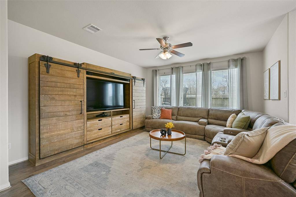 Get cozy and comfortable in this inviting family room at the rear of the home. This space showcases a lighted ceiling fan, luxury vinyl plank floors, neutral paint, & a wall of rear-facing windows shaded by 2-inch blinds and breezy sheer draperies.