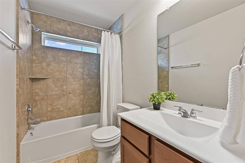 This private en suite bathroom services the previous bedroom and features a cultured marble vanity with a rectangular basin sink, stained wood cabinetry, tile floors, and a combination bathtub and shower with a stone-look tile surround.