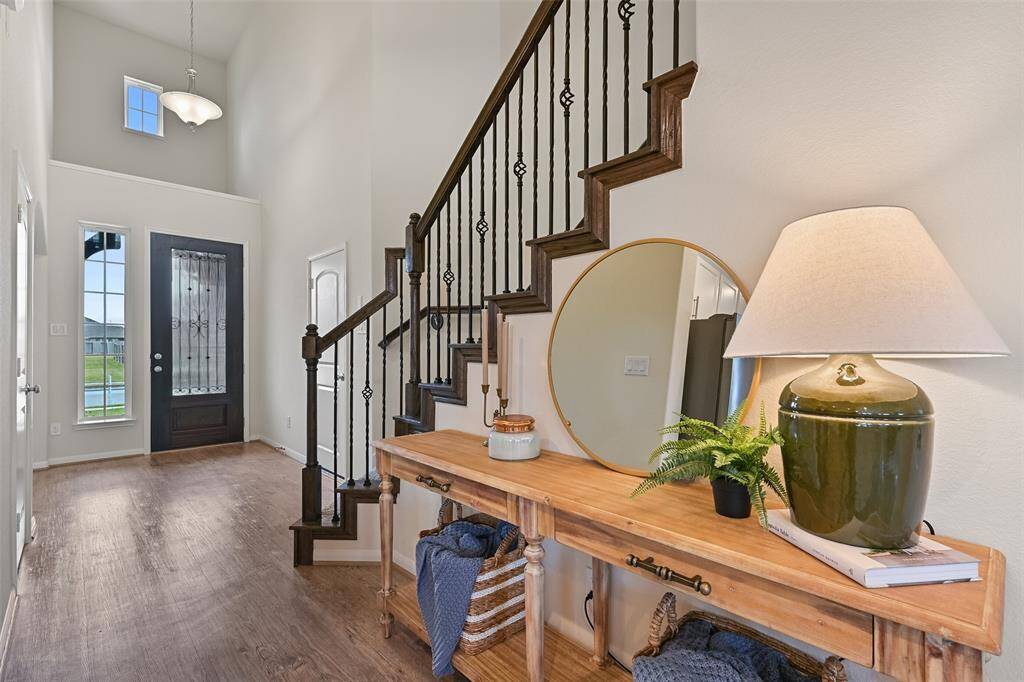 Looking back into the foyer, note the soaring two-story ceiling, seamless luxury vinyl plank floors, an art ledge above the front door, and a sweeping staircase with carpeted treads, wood trim and handrails, and wrought iron basketweave balusters.