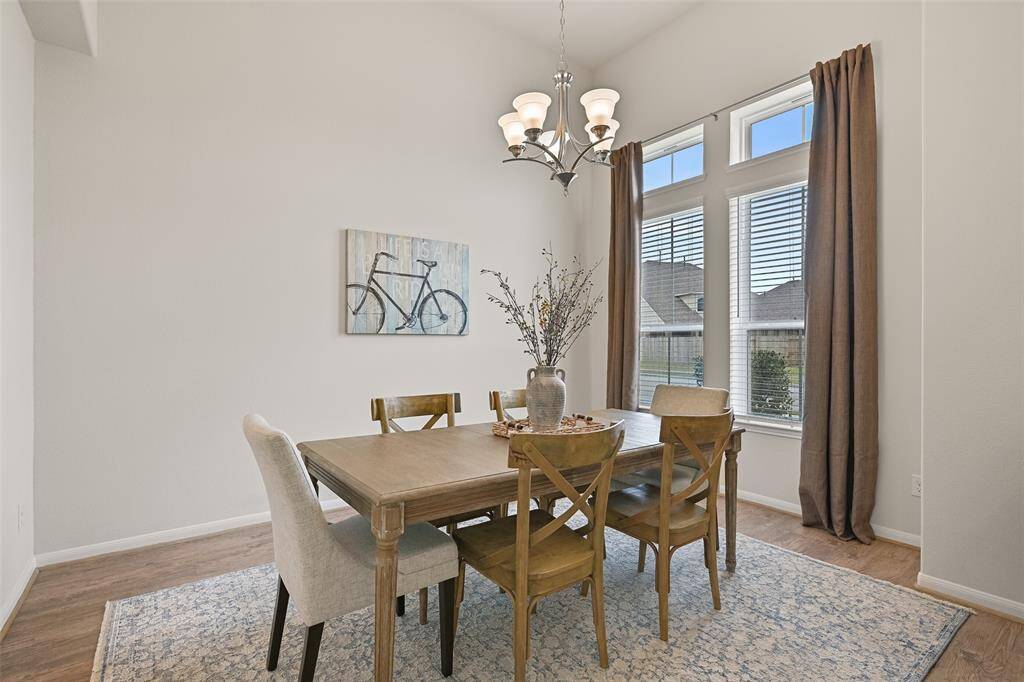 To the right of the foyer, a wide arched entrance leads into this elegant dining room with an elevated 13-foot high ceiling, continued luxury vinyl plank floors, and a pair of front-facing windows dressed with 2-inch blinds and neutral beige draperies.