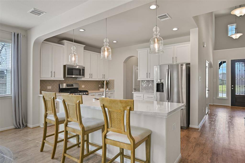 The dining room offers direct access to this centrally located island kitchen that showcases gleaming quartz countertops, a herringbone patterned tile backsplash, white cabinetry with brushed nickel hardware, and a trio of pendant lights above the island with bartop seating space.