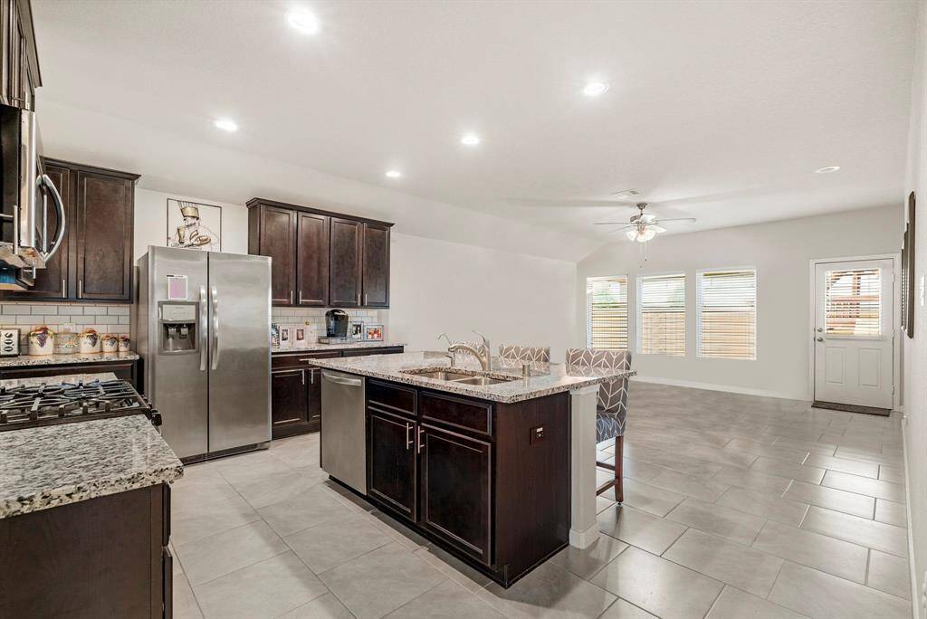 Fall in love with this modern, open-concept kitchen that’s as functional as it is stylish. The space boasts rich espresso cabinetry, gleaming granite countertops, and stainless steel appliances—including a gas range and double-door refrigerator. A large center island with a built-in sink and breakfast bar seating offers the perfect hub for meal prep, casual dining, or entertaining. Recessed lighting, a timeless subway tile backsplash, and expansive sight lines into the living area.