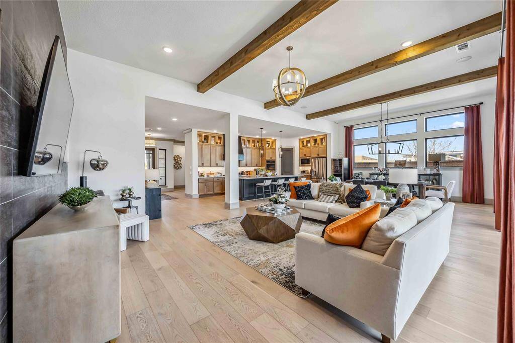 A designer living room with exposed beams and warm tones flows effortlessly into the chef’s kitchen, creating a cohesive space that’s both functional & beautiful.