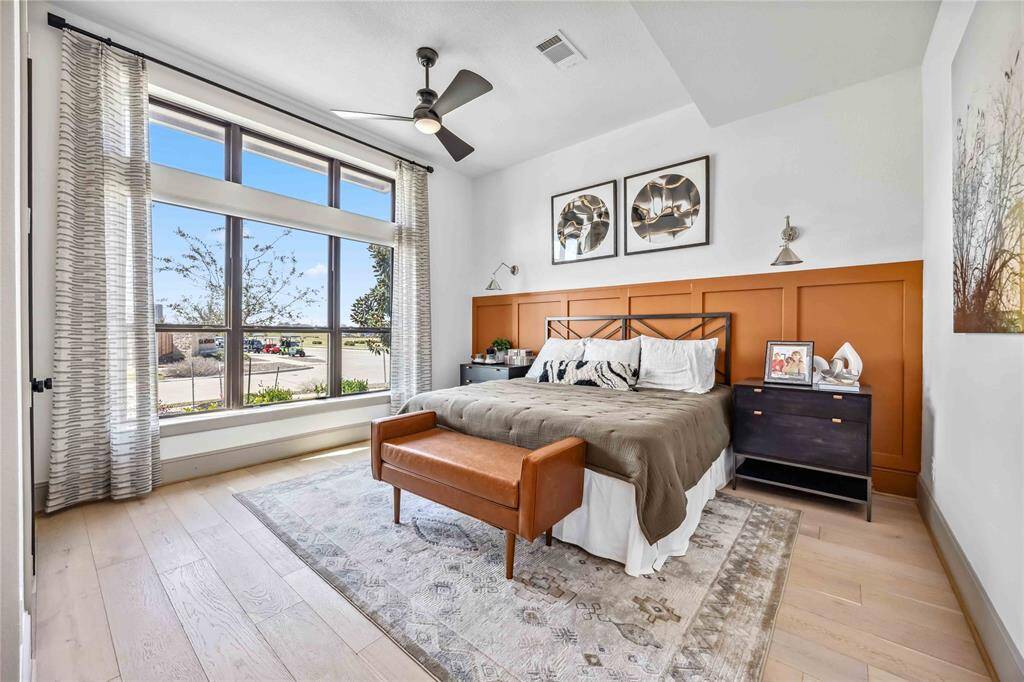 A spacious secondary bedroom on the main floor is filled with natural light from large front-facing windows and features a striking accent wall for added personality.