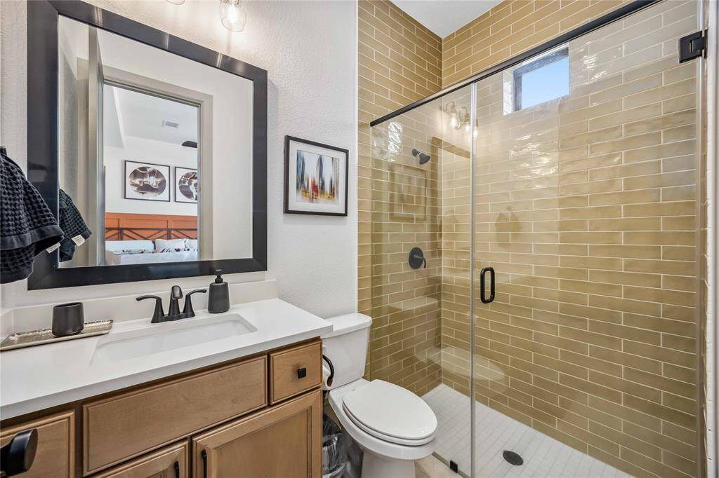 This modern full bathroom features a frameless glass walk-in shower with warm tile surround, matte black fixtures, and sleek vanity with black-framed mirror.