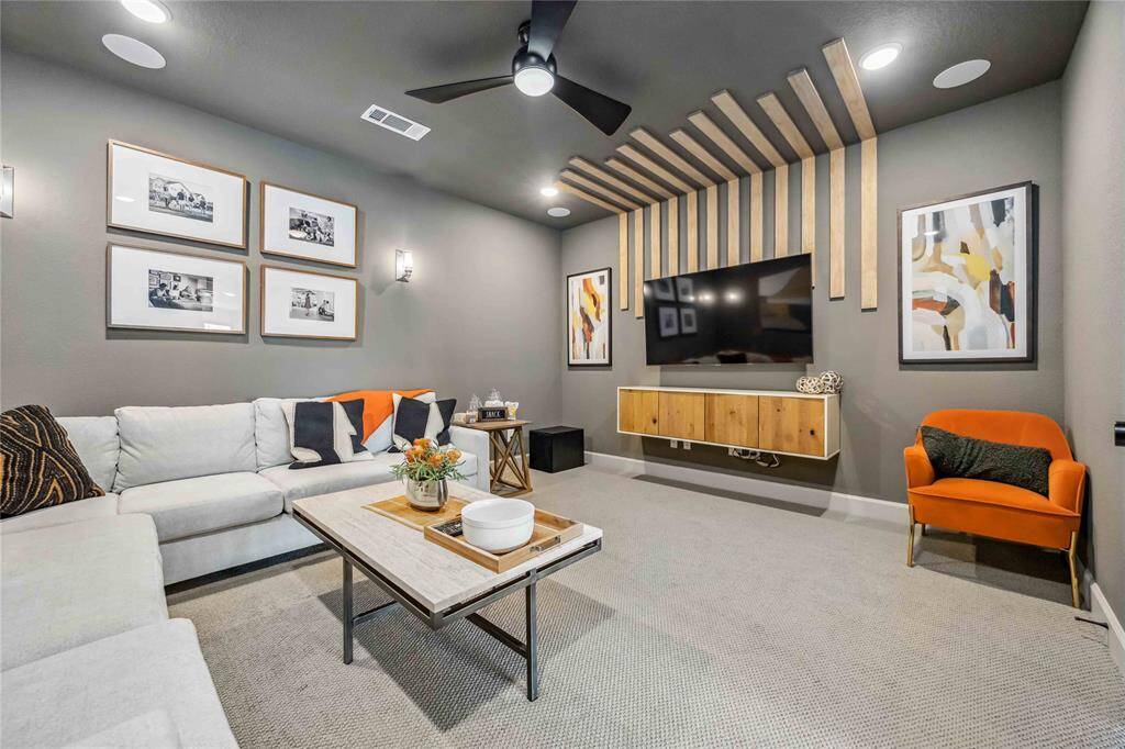 The enclosed media room is designed for comfort with plush carpet, dramatic wall tones, and a custom wood slat feature wall surrounding the mounted TV.