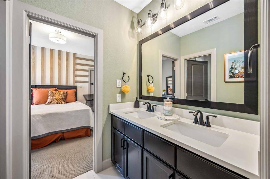 A dual-sink vanity with sleek black cabinetry and modern lighting provides ample space in the well-appointed Jack and Jill bathroom.