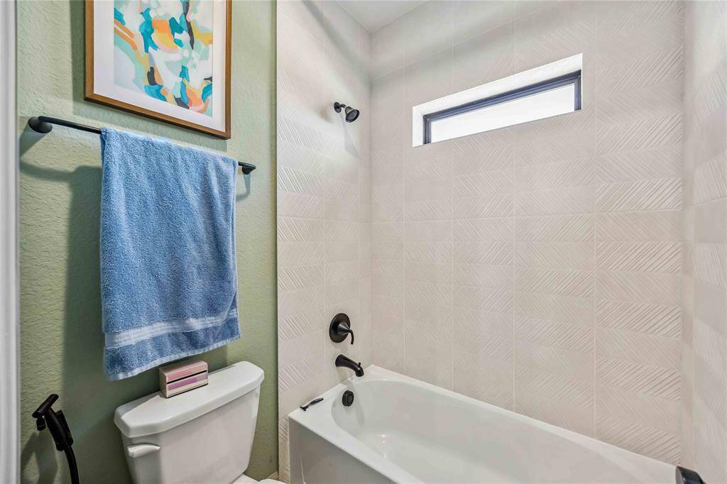 The Jack and Jill bath features a tub/shower combination with stylish textured tile and matte black fixtures, blending form and function beautifully.