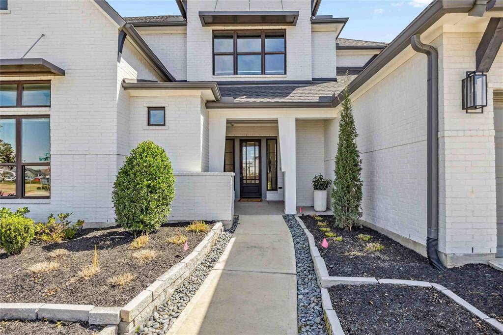 A welcoming front walkway leads to the elegant entry, featuring a modern glass front door and clean, elevated landscaping.