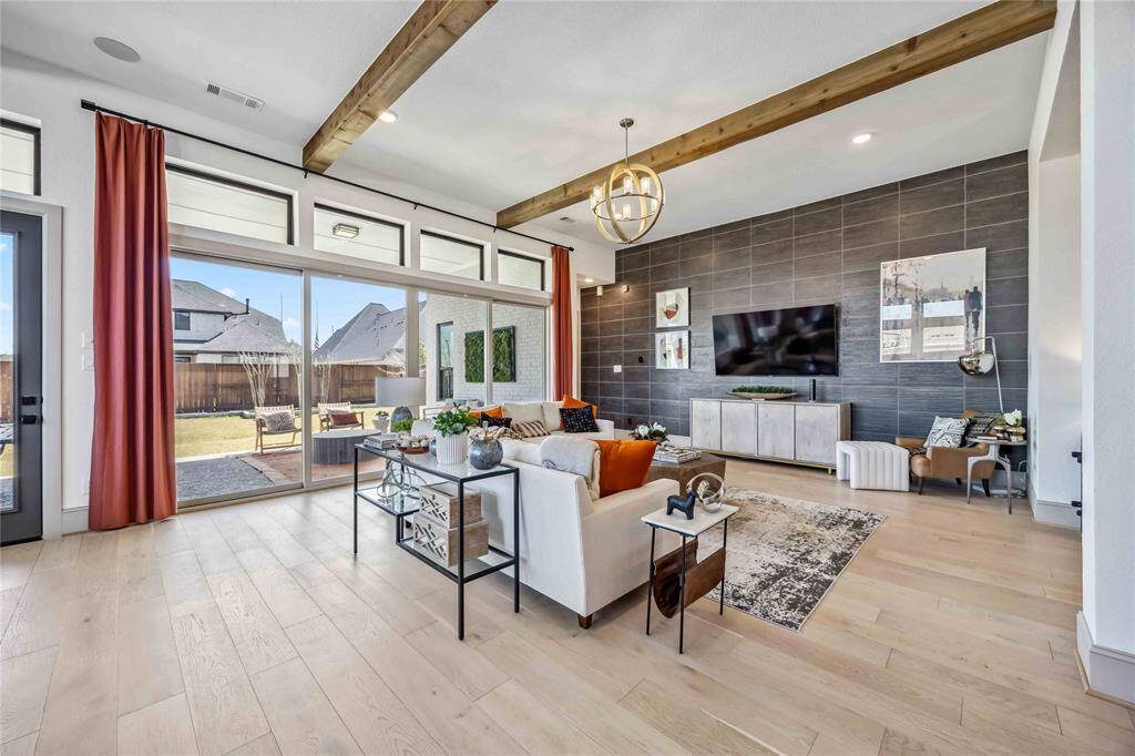 Enjoy abundant natural light and backyard views through a wall of picture windows in this inviting living space, complete with wood beam accents and a striking floor-to-ceiling tile feature wall.