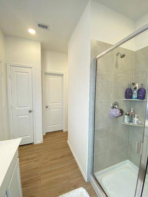 This is a modern bathroom with a walk-in shower, bright lighting, and wood-look flooring. It features clean lines and a neutral color palette.