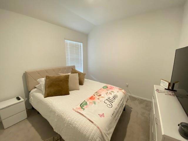 This is a simple, modern bedroom with neutral walls, a window for natural light, and minimal furnishings including a bed and a TV setup.