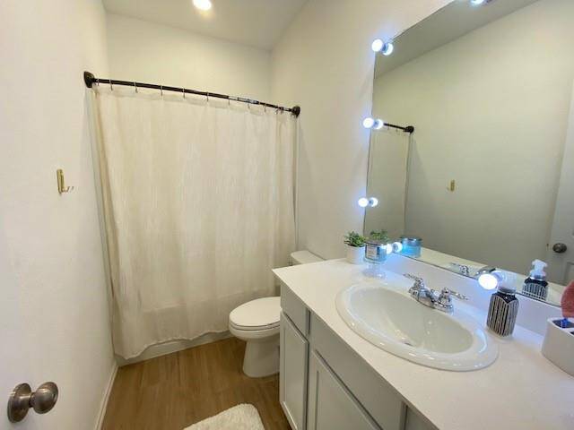 This is a compact, well-lit bathroom featuring a single vanity with a large mirror framed by bright lights, a toilet, and a full-sized bathtub with a privacy curtain. The space has a clean, neutral color scheme.