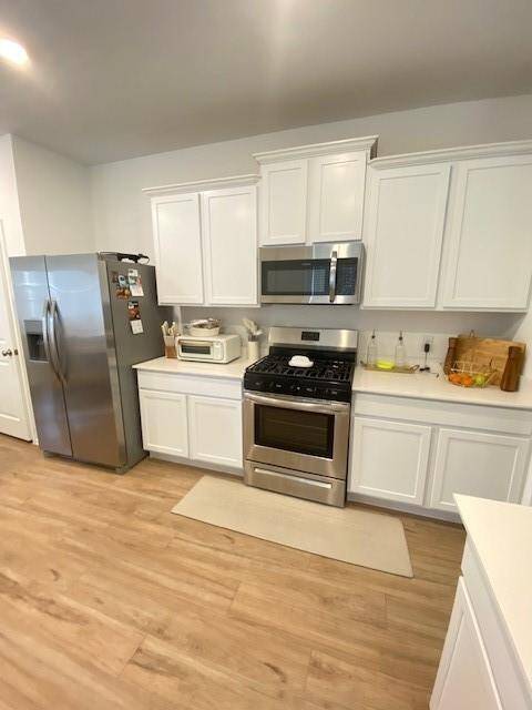This kitchen features modern stainless steel appliances, white cabinetry, and laminate wood flooring, presenting a clean and contemporary space for cooking and dining.