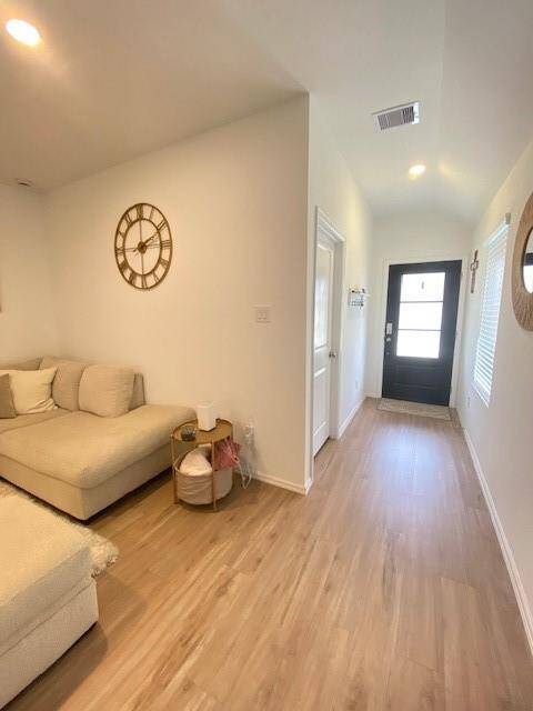 This photo shows a bright, modern entryway that transitions into a cozy living area with light-colored hardwood flooring and neutral walls, complemented by minimalist decor and ample natural light.