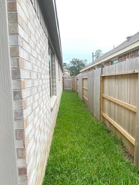 The photo shows a narrow side yard with a well-maintained wooden fence and lush green grass, adjacent to a brick house with vinyl siding. It appears to be a tidy and private space, suitable for a home buyer looking for a secure and low-maintenance outdoor area.
