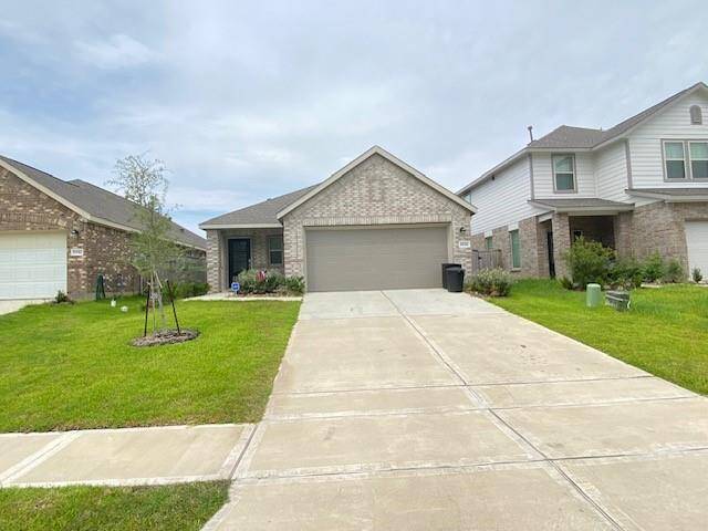 This is a single-story home featuring a brick facade, two-car garage, and a concrete driveway, nestled in a suburban neighborhood with similar style homes. The front yard is well-maintained with young landscaping.