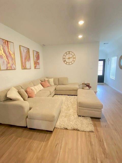 This is a bright and modern living space featuring a large, comfortable sectional sofa, hardwood floors, recessed lighting, and tasteful wall art. A cozy shag rug anchors the seating area, and the room is completed with a simple yet stylish wall clock.