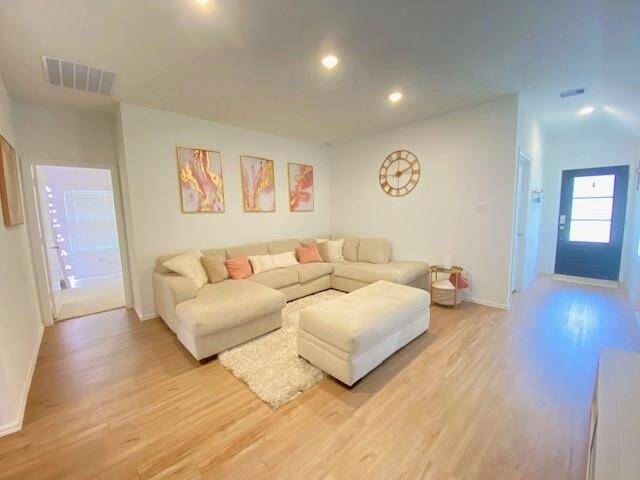 This is a modern and bright living room with a large sectional sofa, hardwood floors, and recessed lighting. The space is accented with contemporary art and a decorative wall clock, providing a welcoming and stylish atmosphere.