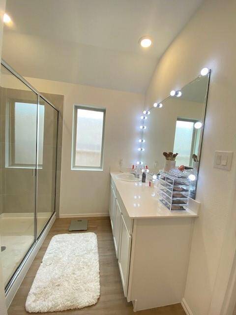 This is a modern, well-lit bathroom featuring a double vanity with a Hollywood-style lit mirror, a glass-enclosed shower, and neutral color tones.