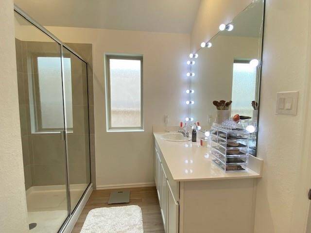 This is a well-lit, modern bathroom featuring a glass-enclosed shower, a single vanity with ample lighting around the mirror, and a frosted window for privacy and natural light.
