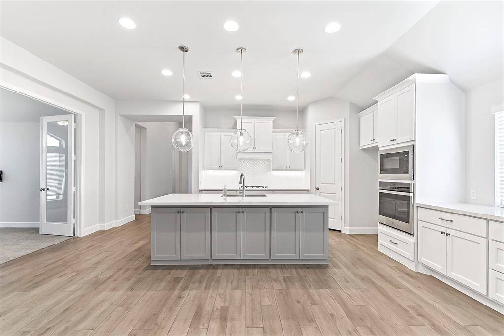 The large, open island kitchen is a chef’s dream, featuring tons of cabinetry and sleek quartz countertops. The space is enhanced with recessed lighting and pendant lights, adding to the home’s abundance of upgrades. To the left, French doors open into an additional living space, perfect for a game room, home office, or any creative use.