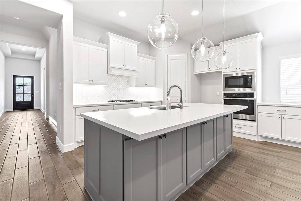 All the common living areas of the home feature beautiful blonde wood-like tile, which runs throughout the entire space. Notice the stunning contrast between the island’s grey and white cabinetry, complemented by extra storage along the breakfast bar.