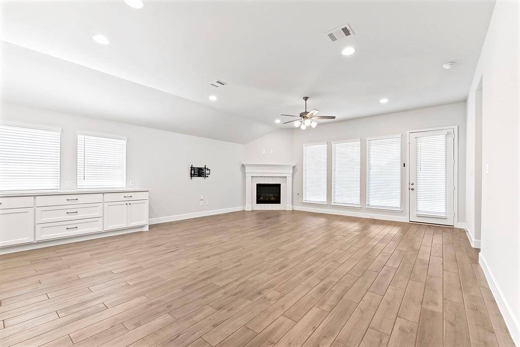 Another view highlights the expansive open living area, showcasing the beautiful wood-look tile flooring, a cozy gas fireplace, and a wall of windows that flood the space with natural light and offer views of the backyard.