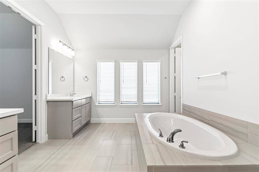 Spacious primary ensuite bathroom featuring dual vanities, a soaking tub, a separate glass-enclosed shower, and generous walk-in closets.