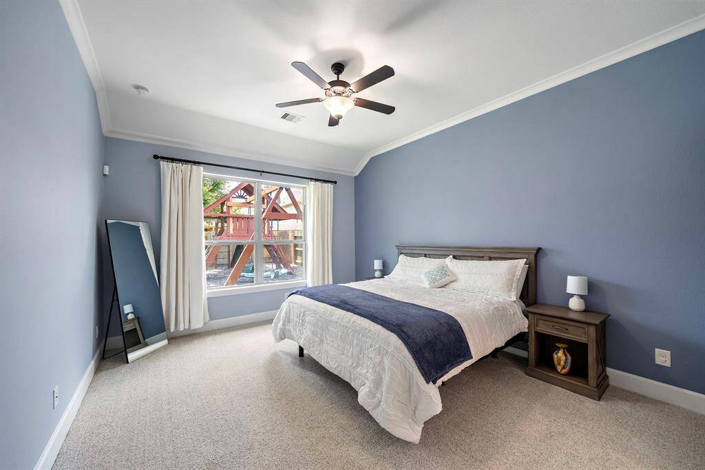 Spacious bedroom with soft luxury carpet, crown molding, ceiling fan, and large window.