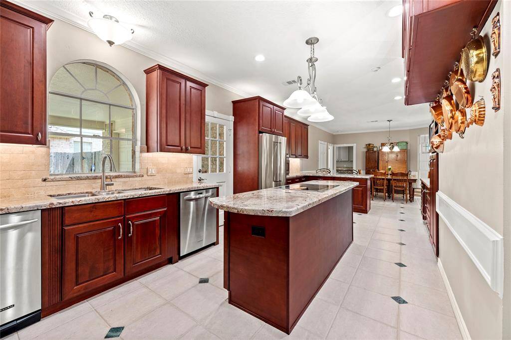 The kitchen boasts custom cherry wooden cabinetry, sleek granite countertops, and stainless-steel appliances including a dishwasher, microwave, and double oven. A central island with induction cooktop also adds functionality and style, while a built-in wine/coffee bar offers a convenient and an entertainer's touch. The spacious layout flows seamlessly into the adjacent breakfast area—perfect for everyday living and entertaining.