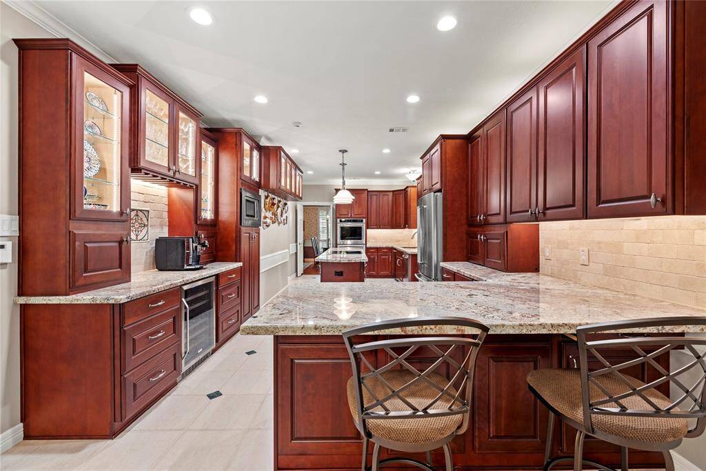 This kitchen features rich wooden cabinetry, granite countertops, and ample storage. It includes modern appliances, a built-in oven, and a kitchen island with seating, offering a spacious and inviting cooking and dining area.