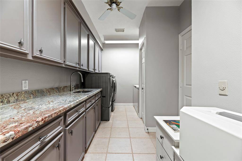 Spacious laundry room with ample storage including two closets, upper and lower cabinets storage space, granite countertops, undermount stainless steel sink, and tile flooring. It creates a clean, functional space ideal for household tasks.  Room for a extra fridge or freezer.