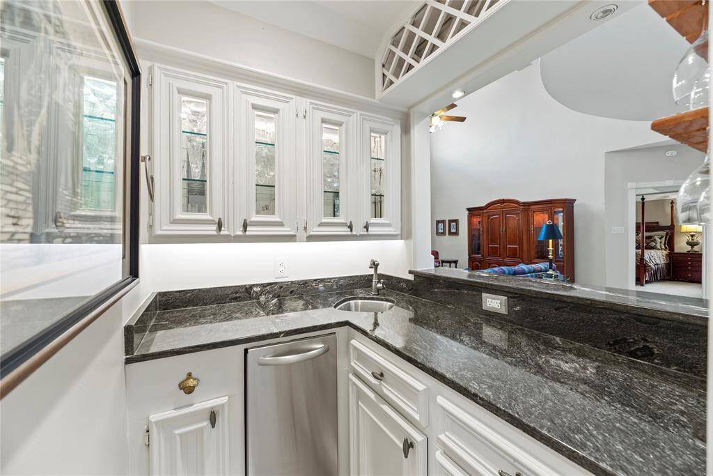 The centrally located wet bar area with sleek black granite countertops, white cabinetry, and a built-in sink. It's open to a spacious family room, providing a seamless flow for entertaining.
