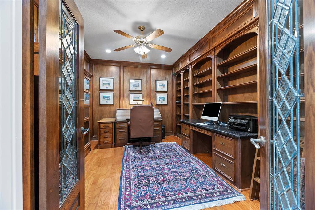 The home office showcases rich wood paneling, built-in bookshelves, a dedicated desk area, and a ceiling fan—creating a warm, sophisticated, and highly functional workspace ideal for productivity.  The antique leaded glass double entry doors to the study are from Morton's Antiques in New Orleans, installed by Mills Custom Doors.