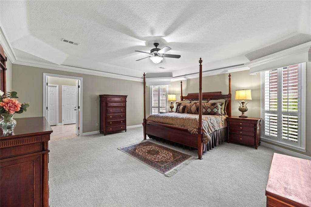 The spacious primary bedroom, located on the first floor, features carpet flooring, a ceiling fan, and windows that allow natural light to brighten the space. It includes a private en-suite bathroom and a spacious walk-in closet for added comfort and convenience.