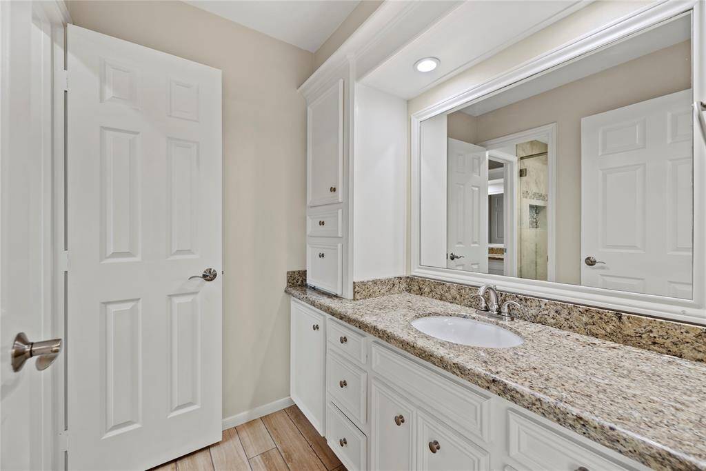 This bathroom features a spacious granite countertop with an undermount sink, ample cabinet storage, and a large mirror. The neutral color palette and recessed lighting create a bright and welcoming atmosphere.