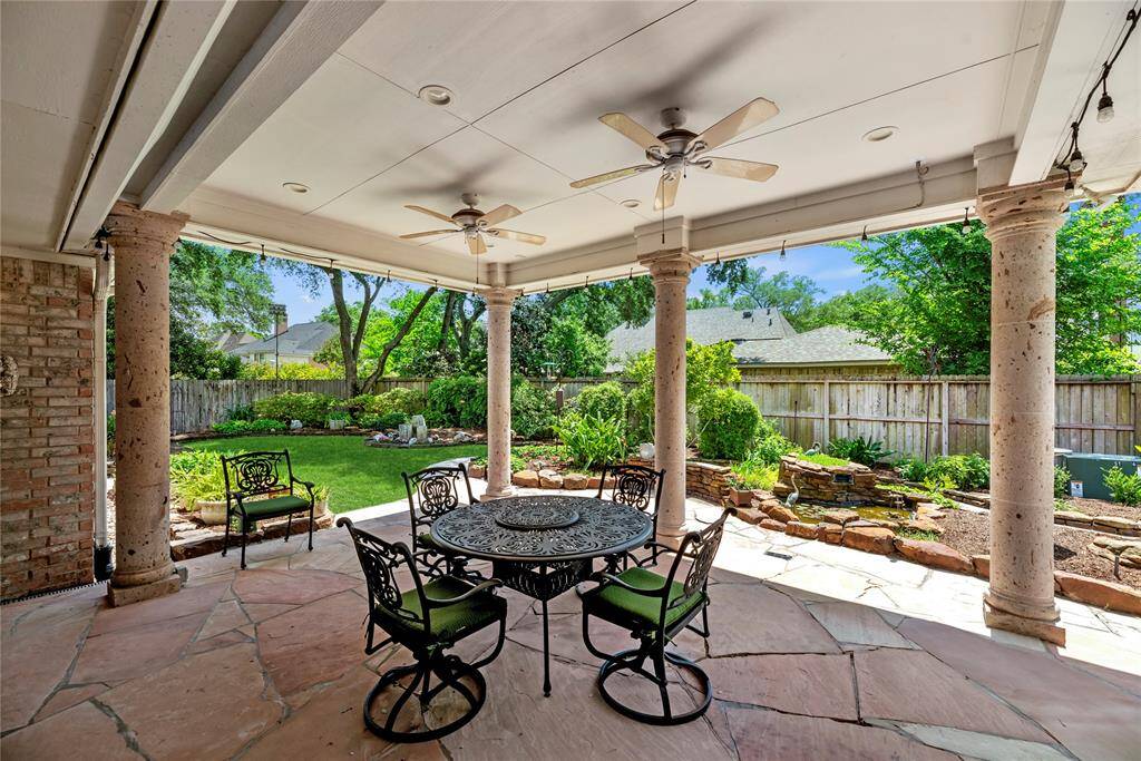 The spacious, covered patio features ceiling fans and overlooks a beautifully landscaped garden, creating the perfect setting for relaxation or enjoying the outdoors in a serene space.
