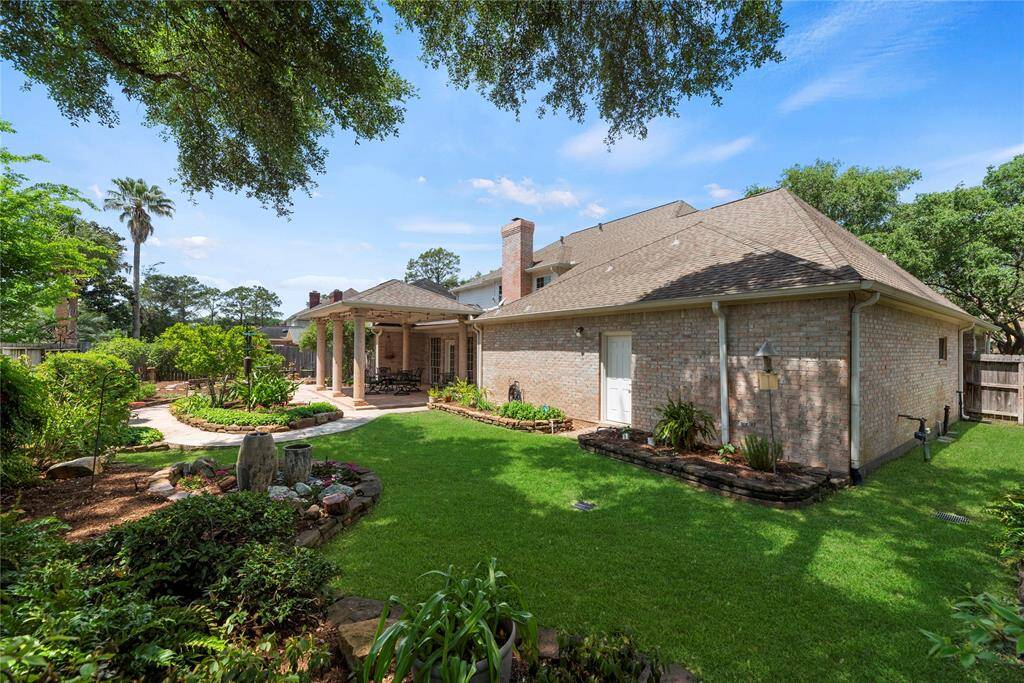 Spacious backyard featuring a well-maintained garden and a covered patio, perfect for outdoor dining and relaxation. The brick exterior adds a timeless, classic touch to the home, enhancing the overall charm of the space.